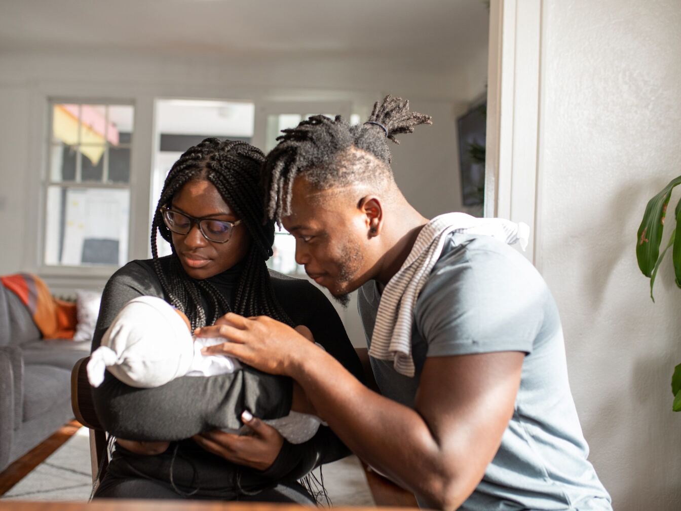 A mother holds her newborn in a white knit cap while the father leans in close.