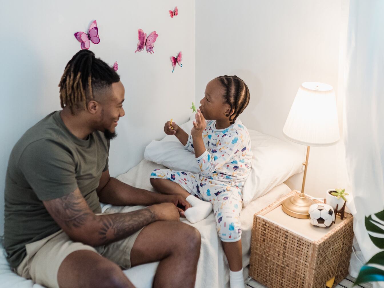 A small child in pajamas sits on the bed at bedtime, telling their smiling father a story.